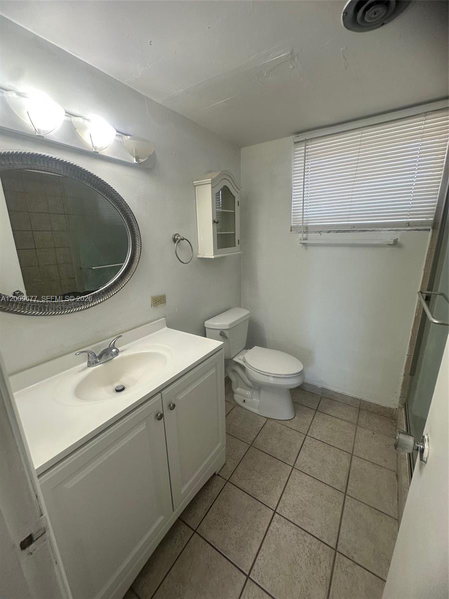 A bathroom features a white vanity, a round mirror, a toilet, and a tiled floor — 1530 NE 191st St # 205, Miami FL 33179, MIAMI, FL
