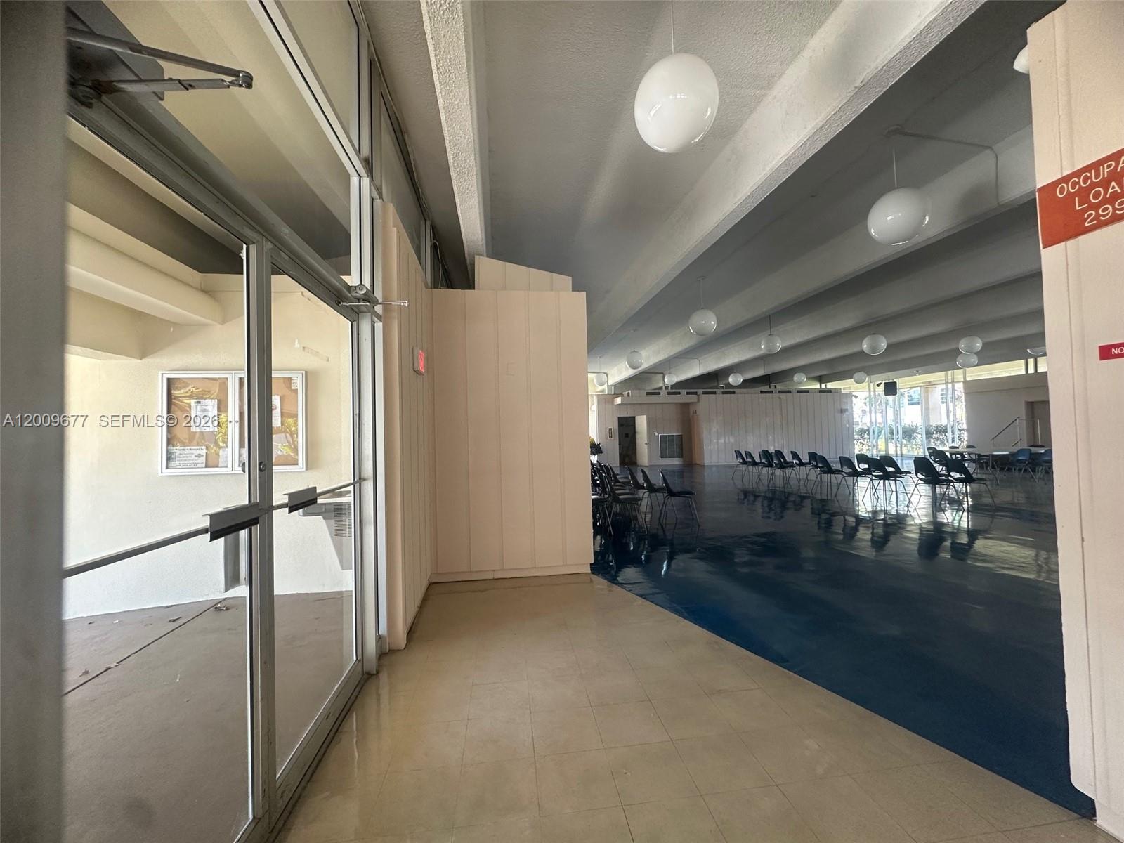 A large, open-concept community room features a blue floor, rows of chairs, and globe lighting — 1530 NE 191st St # 205, Miami FL 33179, MIAMI, FL
