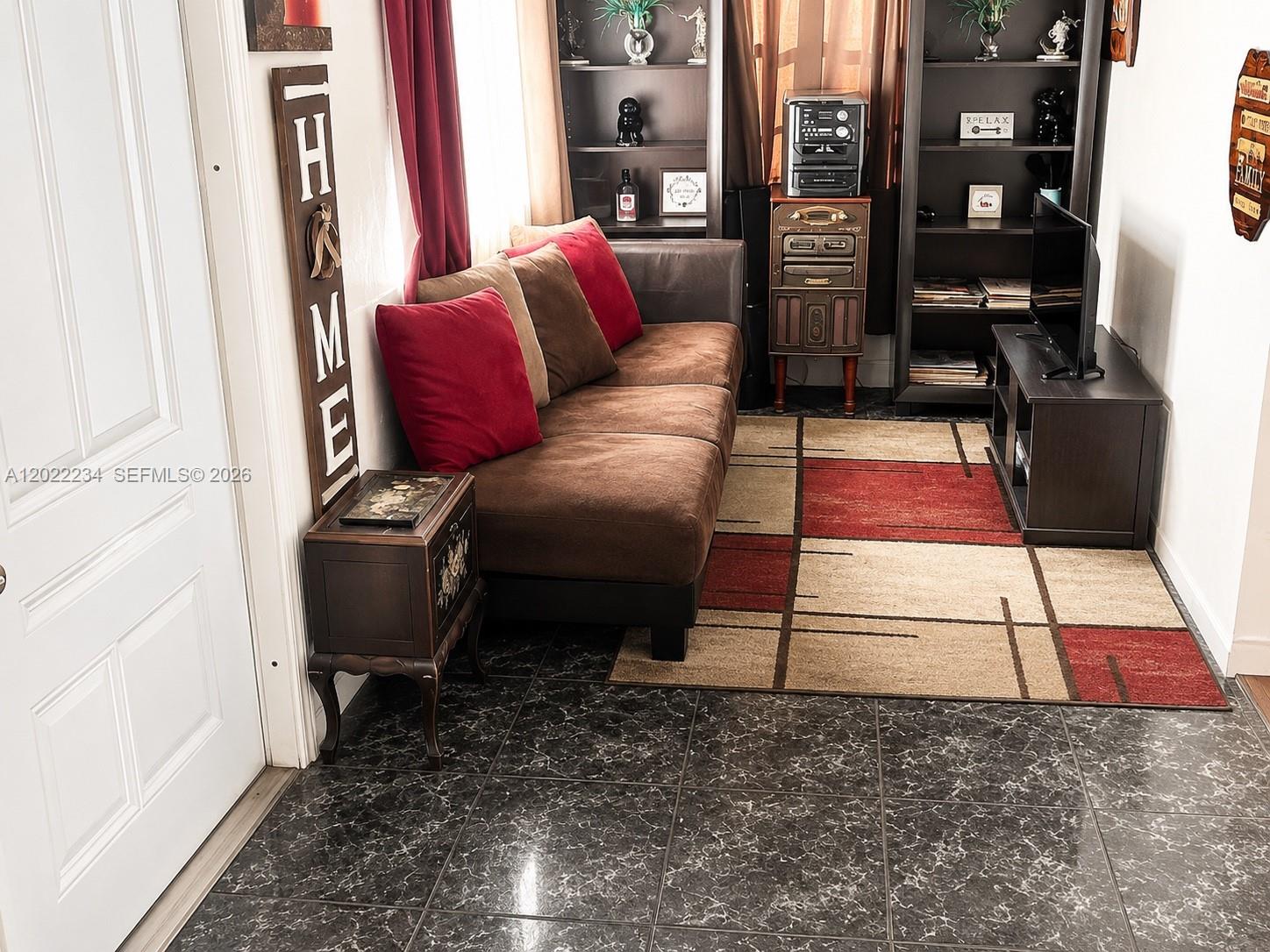 A living room features a brown sofa, a patterned area rug, and dark shelving units — 716 NW 4th St, Hallandale Beach FL 33009, HALLANDALE BEACH, FL