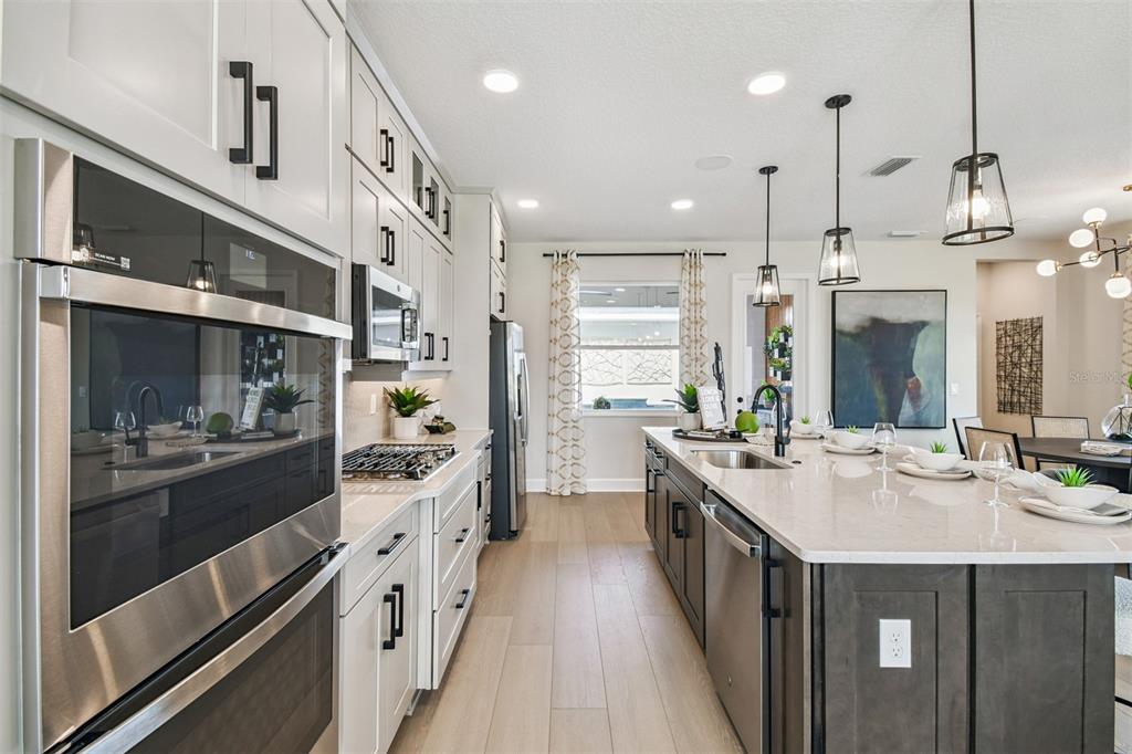 A modern kitchen features white upper cabinets, dark lower cabinets, a large island, and stainless appliances — 17106 BEACHGRASS ALLEY, WINTER GARDEN, FL
