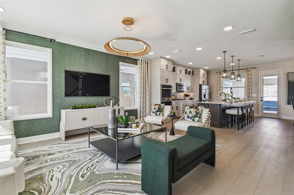 An open-concept living room and kitchen feature a green accent wall and wood-look flooring — 17106 BEACHGRASS ALLEY, WINTER GARDEN, FL