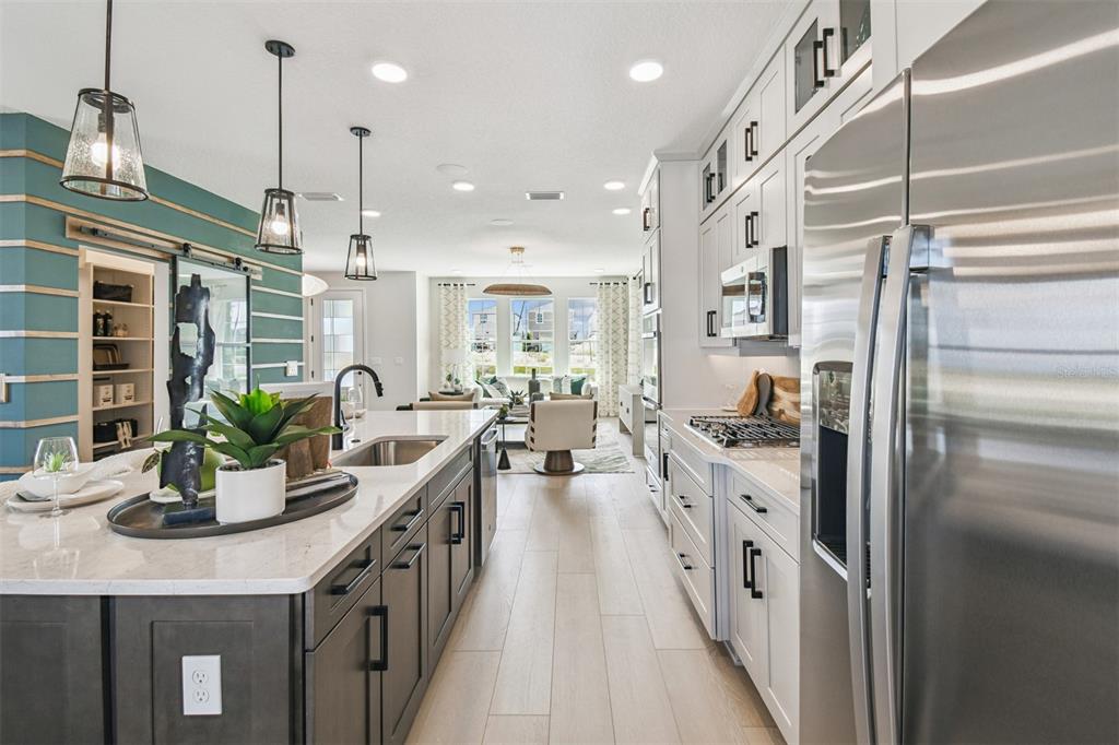 A modern kitchen features a dark island, white cabinetry, stainless steel appliances, and wood flooring — 17106 BEACHGRASS ALLEY, WINTER GARDEN, FL