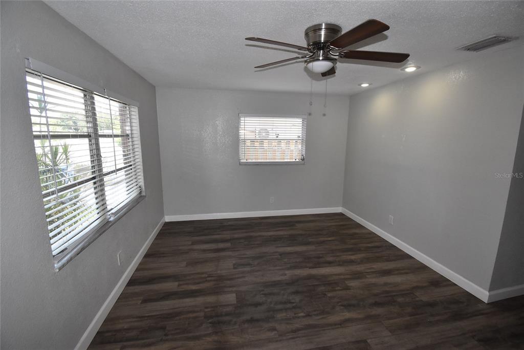 An empty room features gray walls, dark wood-look flooring, a ceiling fan, and two windows — 2713 26TH AVENUE N, ST PETERSBURG, FL