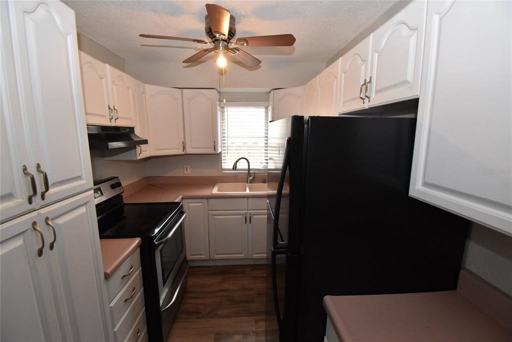 A kitchen features white cabinets, pink countertops, black appliances, and wood-look flooring — 2713 26TH AVENUE N, ST PETERSBURG, FL