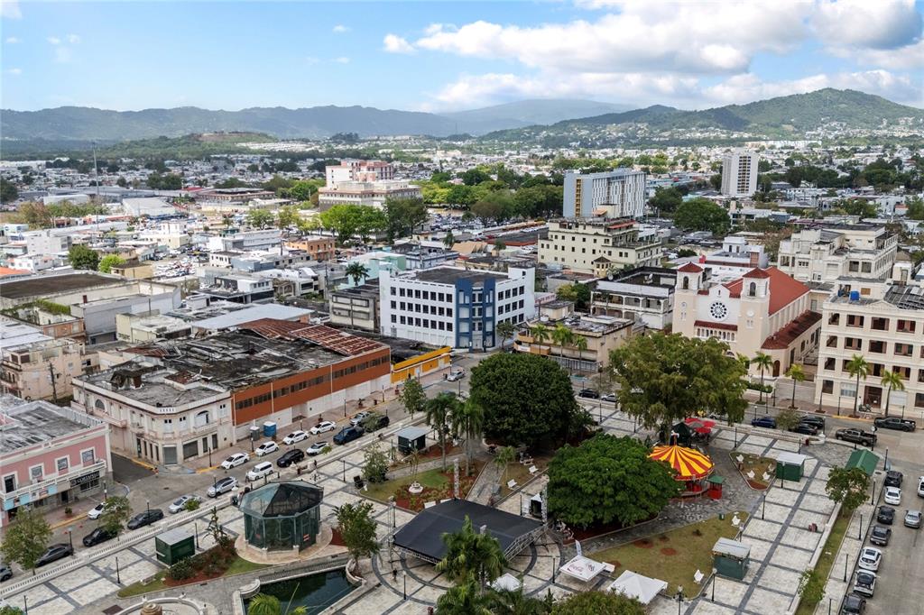 An aerial view of a city plaza featuring a gazebo, trees, and surrounding buildings — 48 ESQUINA CORCHADO Y RUIZ BELVIS, CAGUAS, PR