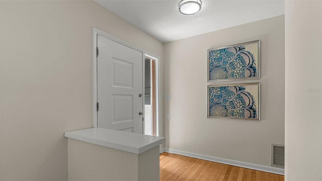 An entryway features a white door, hardwood floors, and two framed abstract art pieces — 1114 NW 36TH DRIVE, GAINESVILLE, FL