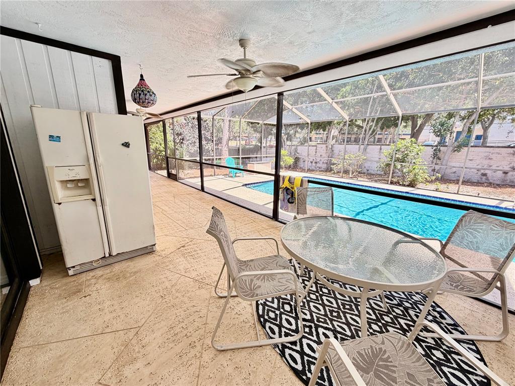 A screened-in patio features a glass dining table, a white refrigerator, and a swimming pool — 1382 SUTTON PLACE DRIVE, PALM HARBOR, FL