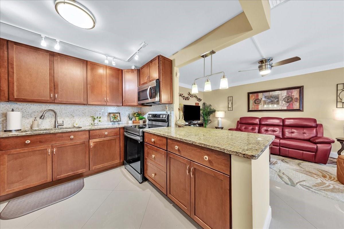 A kitchen with wood cabinets and granite countertops opens into a living room with red furniture — 2047 Wolverton C # 2047, Boca Raton FL 33434, BOCA RATON, FL