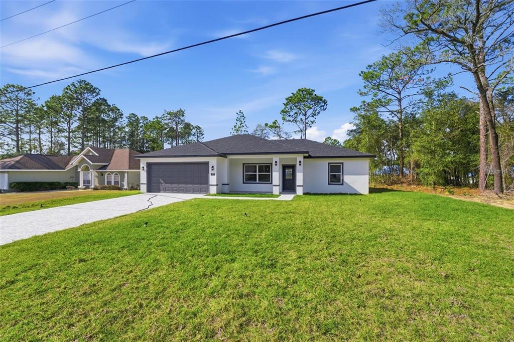 A single-story white house with a dark roof and a two-car garage sits on grass — 2275 W LINDEN DRIVE, CITRUS SPRINGS, FL