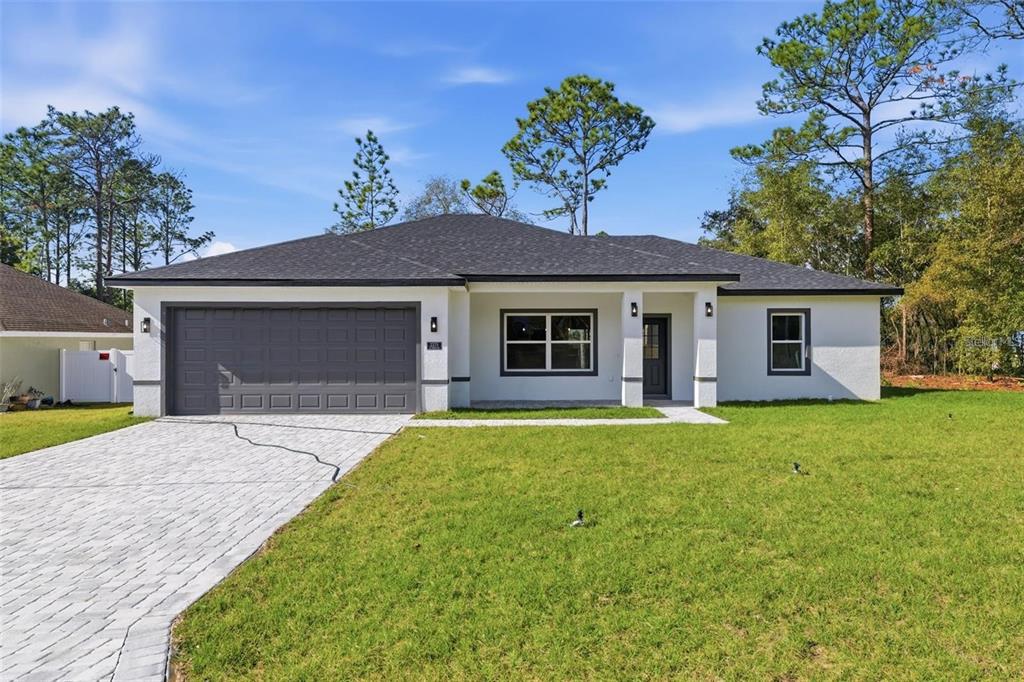 A single-story house with a gray garage door, white stucco exterior, and a paved driveway — 2275 W LINDEN DRIVE, CITRUS SPRINGS, FL