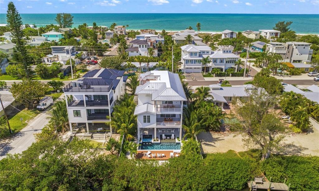 An aerial view shows two modern multi-story houses with pools near a beach — 404 NORTH SHORE DR, ANNA MARIA, FL