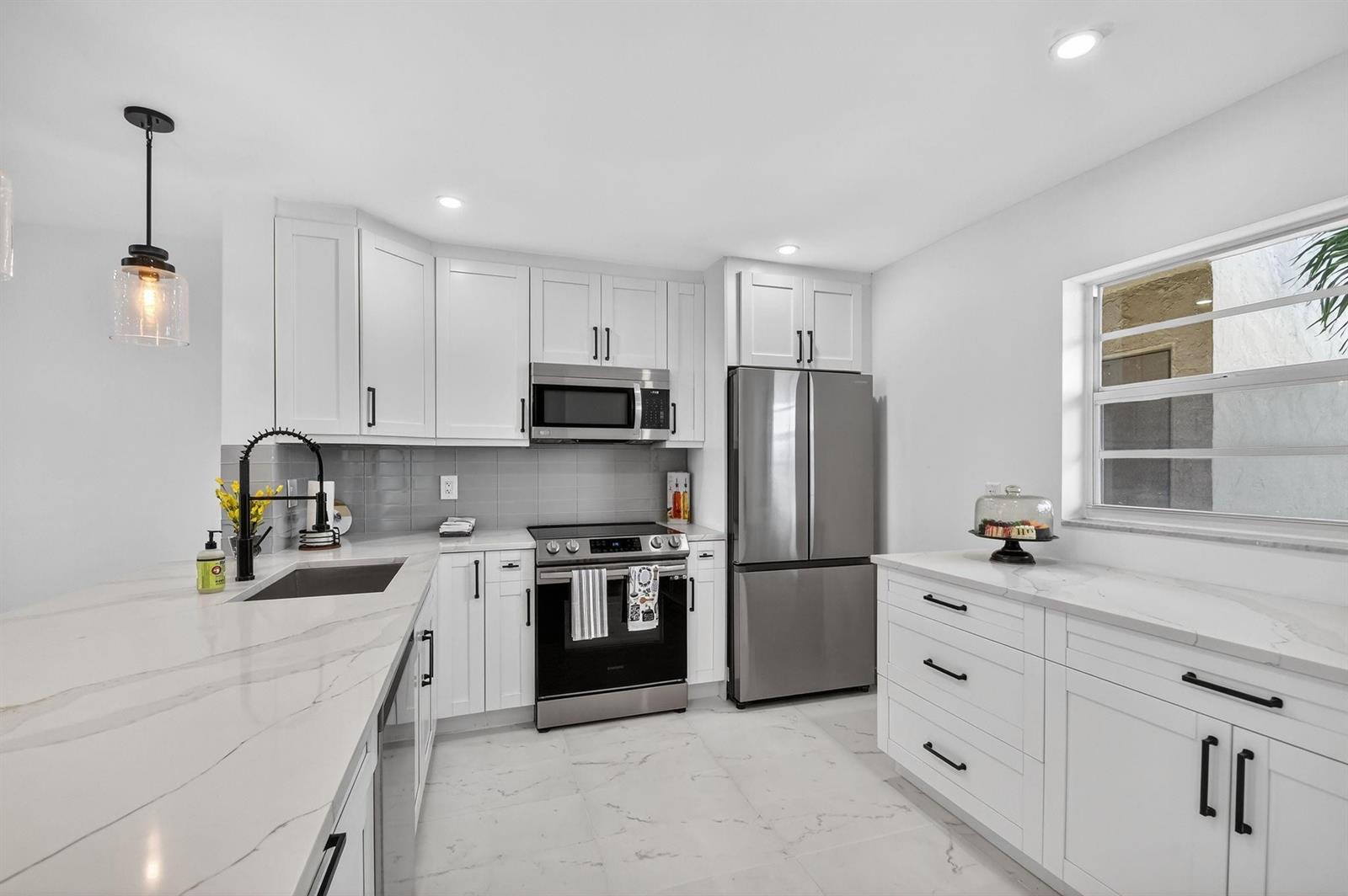A modern kitchen features white cabinets, stainless steel appliances, and marble-look countertops and flooring — 2300 NE 1st Lane # 201, Boynton Beach FL 33435, BOYNTON BEACH, FL