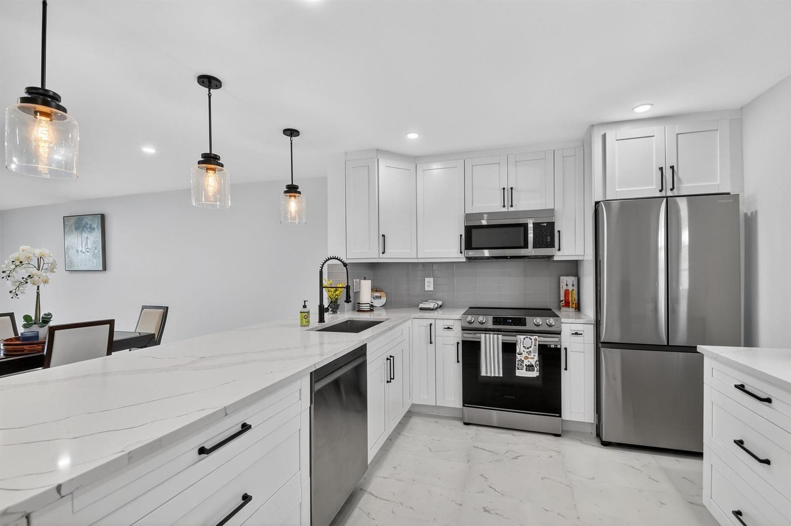 A modern kitchen features white cabinets, stainless steel appliances, and a marble-patterned countertop island — 2300 NE 1st Lane # 201, Boynton Beach FL 33435, BOYNTON BEACH, FL