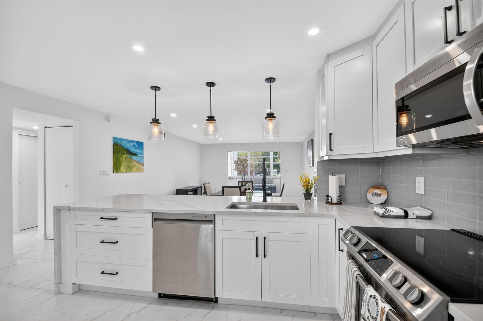 A modern kitchen features white cabinets, stainless steel appliances, marble countertops, and three pendant lights — 2300 NE 1st Lane # 201, Boynton Beach FL 33435, BOYNTON BEACH, FL