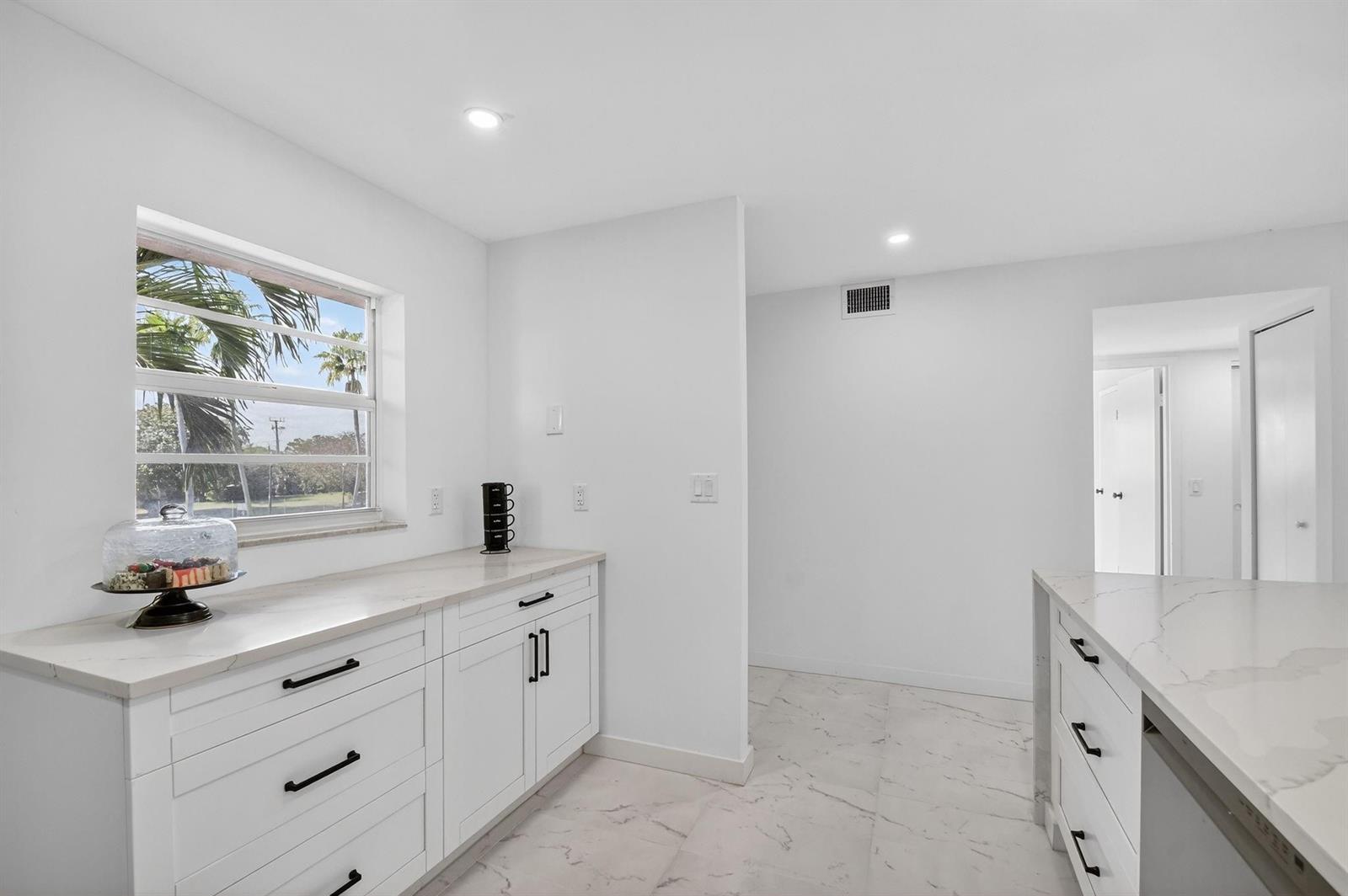 A bright kitchen features white cabinets, marble-style countertops, and a window overlooking palm trees — 2300 NE 1st Lane # 201, Boynton Beach FL 33435, BOYNTON BEACH, FL