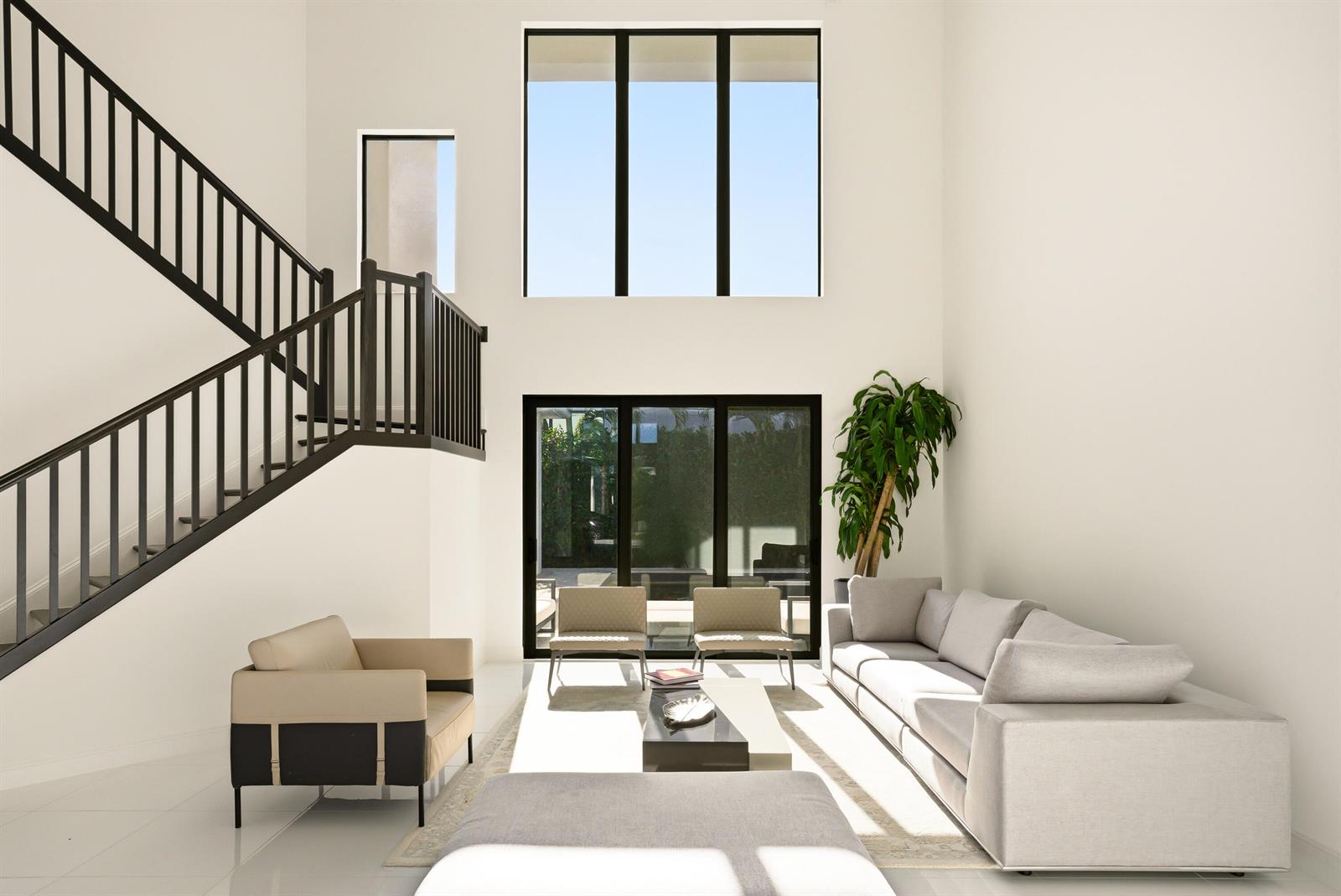A bright living room features a high ceiling, a staircase, and large windows overlooking outdoors — 6990 NW 27th Avenue, Boca Raton FL 33496, BOCA RATON, FL