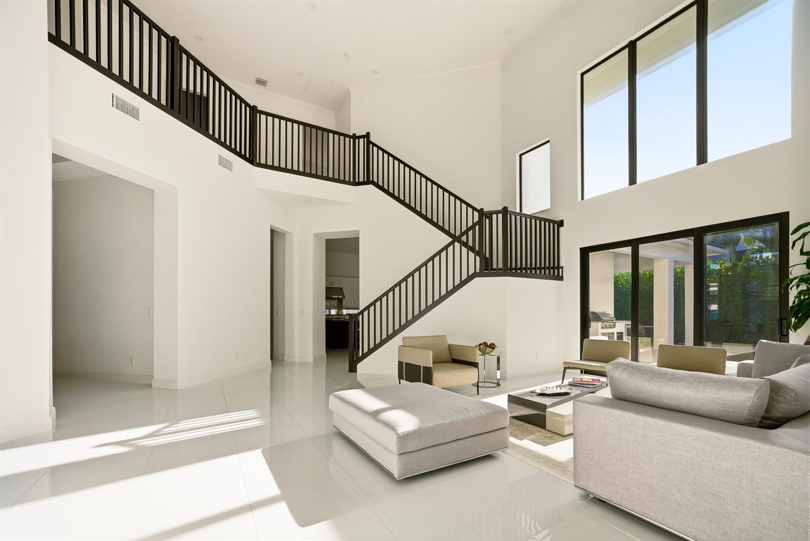 A spacious living room features white tile floors, a grand staircase, and floor-to-ceiling windows — 6990 NW 27th Avenue, Boca Raton FL 33496, BOCA RATON, FL