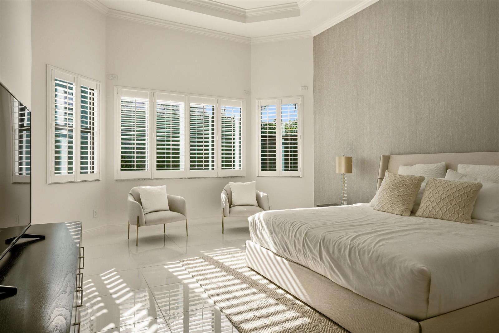 A bright bedroom features a large bed, two armchairs, white tile floors, and plantation shutters — 6990 NW 27th Avenue, Boca Raton FL 33496, BOCA RATON, FL