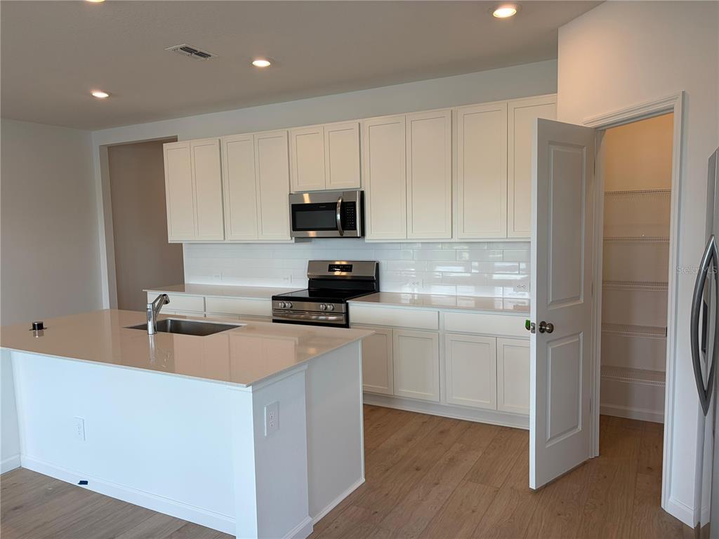 A modern kitchen features white cabinets, stainless steel appliances, a center island, and wood flooring — 5548 MORANT BAY PATH UNIT B, KISSIMMEE, FL