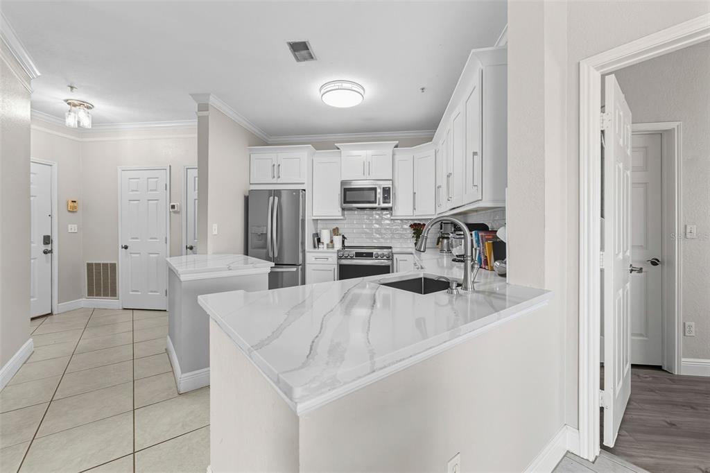 A kitchen features white cabinetry, stainless steel appliances, and a white marble-look countertop peninsula — 4333 BAYSIDE VILLAGE DRIVE UNIT 304, TAMPA, FL