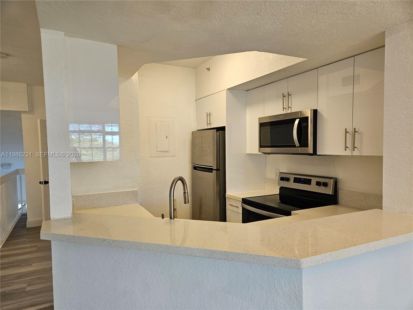A kitchen features white cabinets, stainless steel appliances, and a light-colored quartz breakfast bar — 751 SW 148th Ave # 1012, Sunrise FL 33325, SUNRISE, FL
