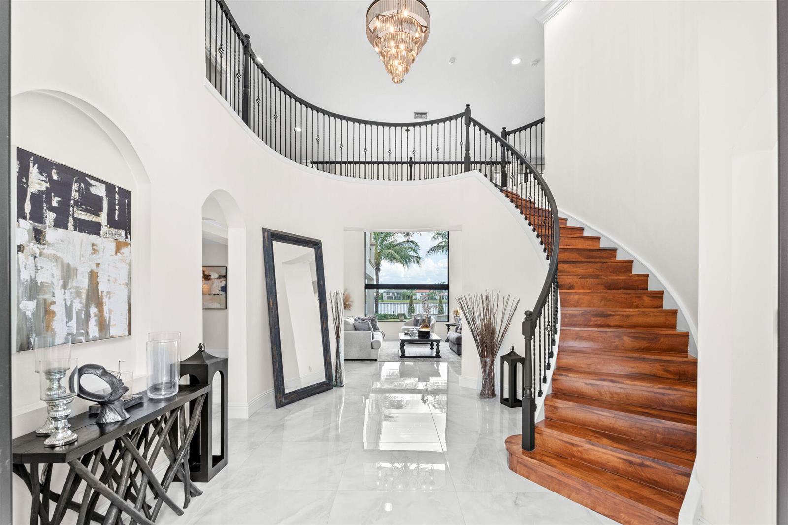 A grand foyer features a curved wooden staircase, white marble floors, and a crystal chandelier — 647 Edgebrook Lane, Royal Palm Beach FL 33411, ROYAL PALM BEACH, FL