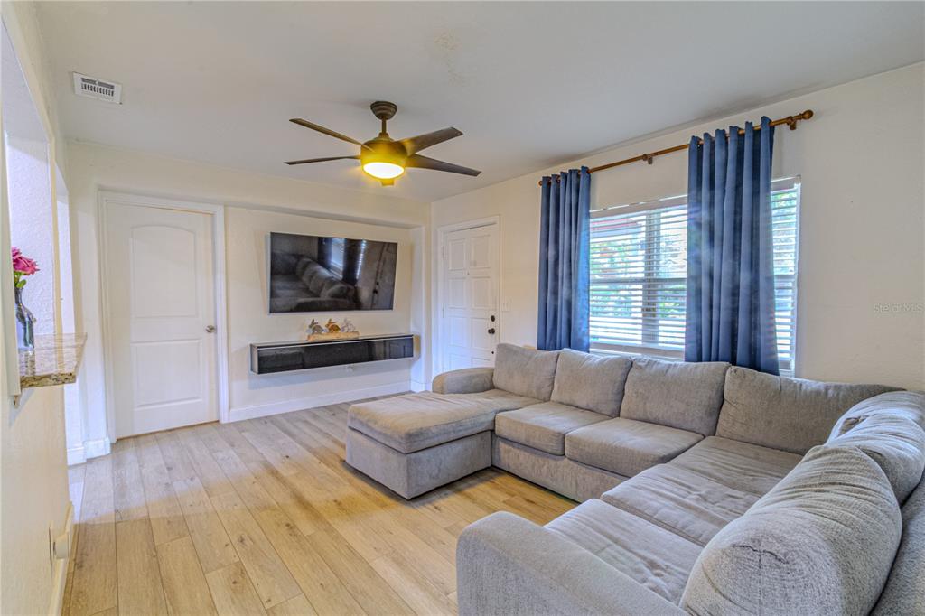 A living room features a sectional sofa, a wall-mounted television, and wood-look flooring — 1026 SARITA STREET, SANFORD, FL