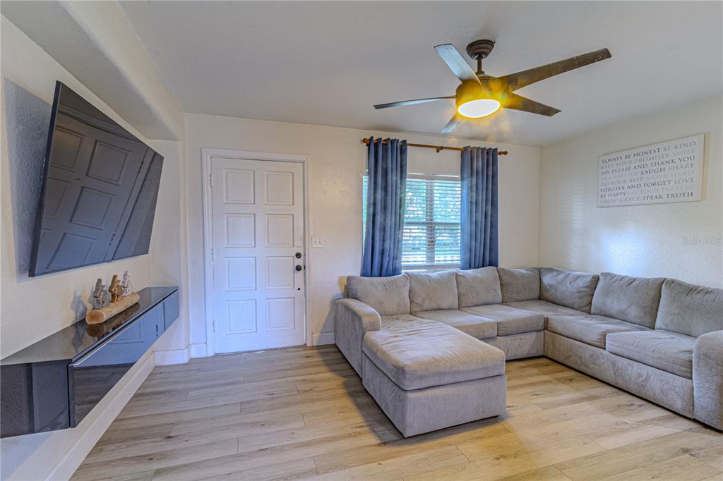 A living room features a gray sectional sofa, a wall-mounted television, and wood-look flooring — 1026 SARITA STREET, SANFORD, FL