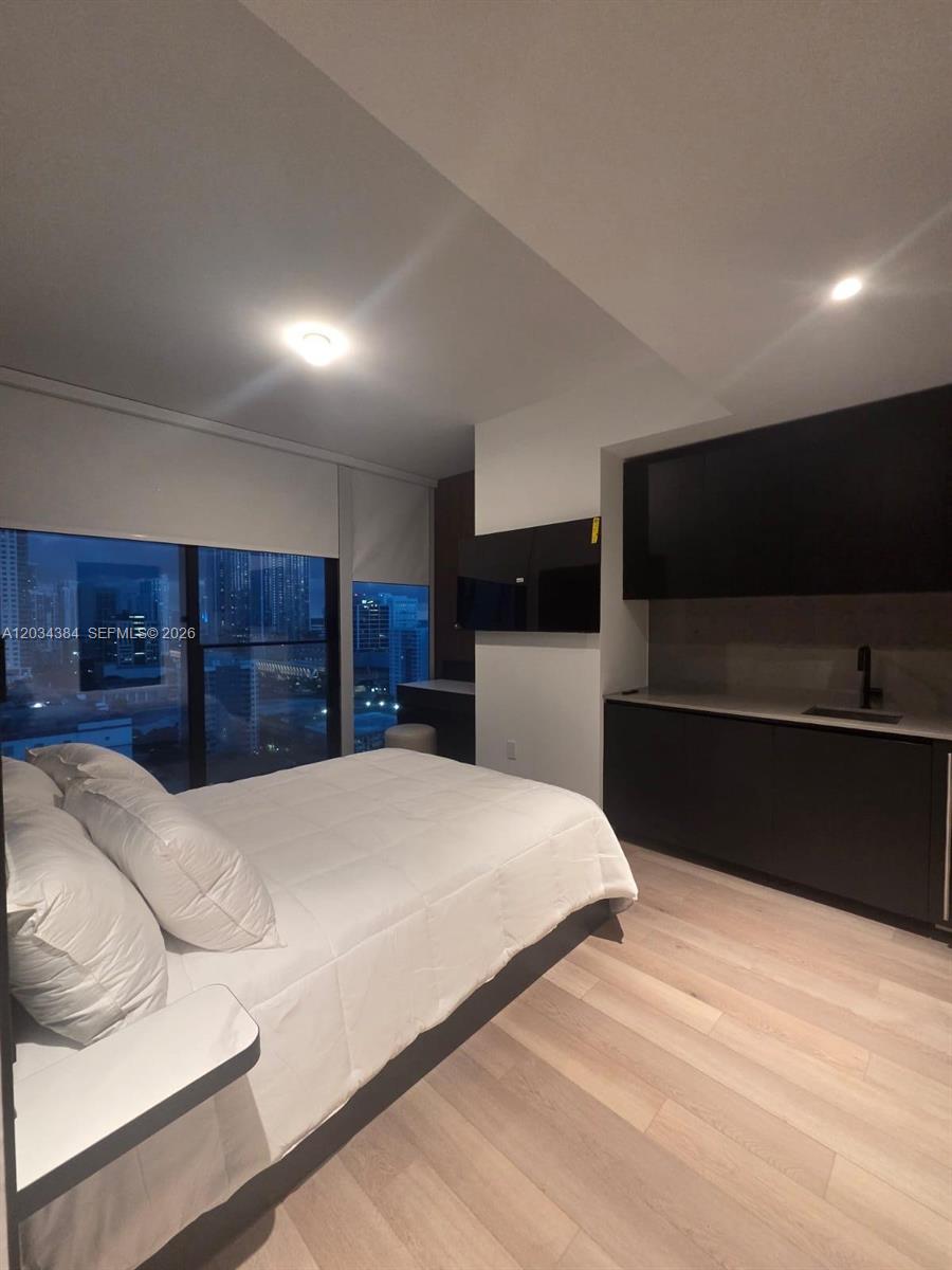 A modern bedroom features a white bed, light wood flooring, and a dark kitchenette area — 20 NE 11 # 2208, South Miami FL 33132, SOUTH MIAMI, FL