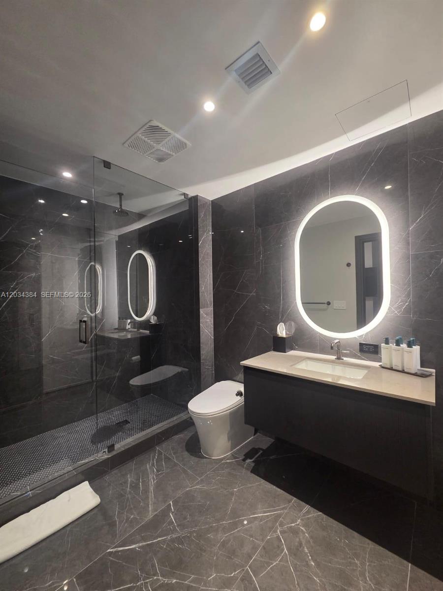 A modern bathroom features dark marble-style tiling, a glass-enclosed shower, and a backlit oval mirror — 20 NE 11 # 2208, South Miami FL 33132, SOUTH MIAMI, FL