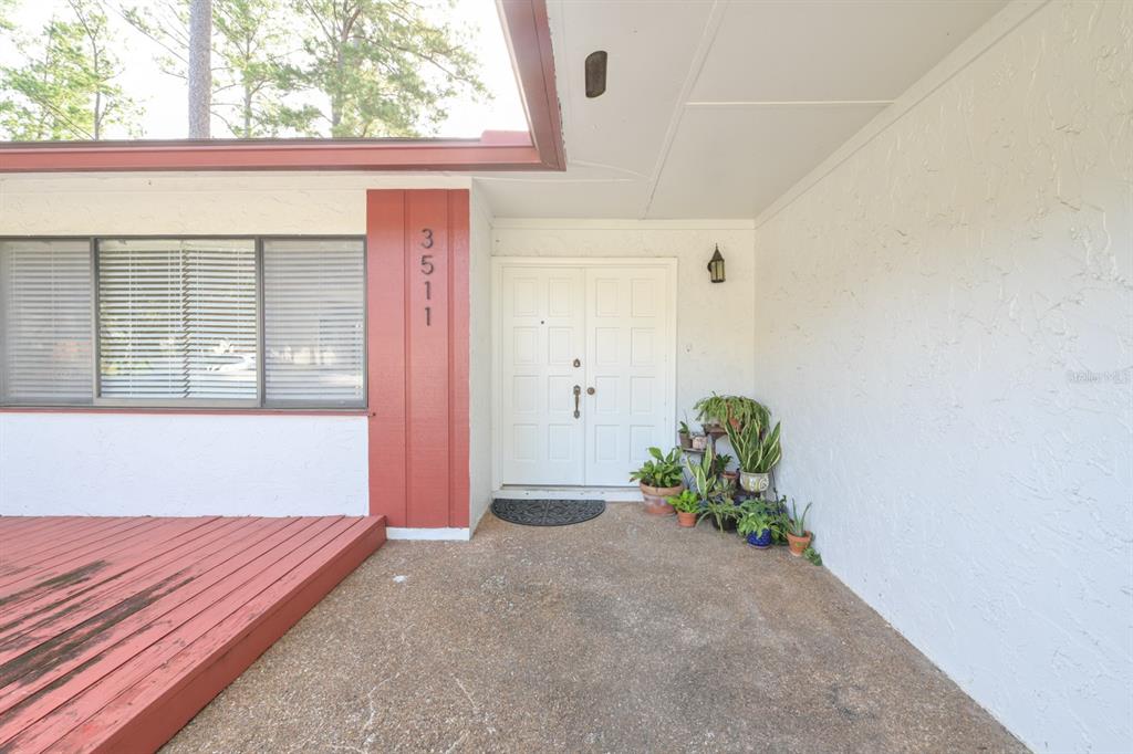 A white double door entrance features a red accent wall and a wooden deck — 3511 NW 40TH TERRACE, GAINESVILLE, FL