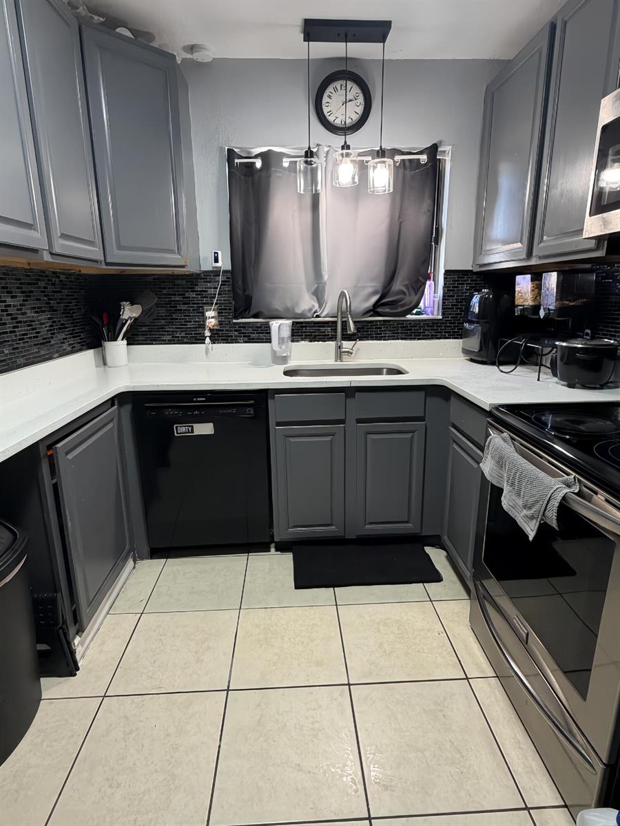 A kitchen features gray cabinets, white countertops, a black tile backsplash, and stainless steel appliances — 190 Abalone Road NW, Palm Bay FL 32907, PALM BAY, FL