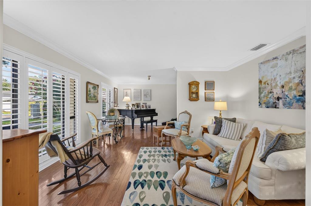 A living room with hardwood floors, a grand piano, a white sofa, and plantation shutters — 823 WOODS COURT, MAITLAND, FL
