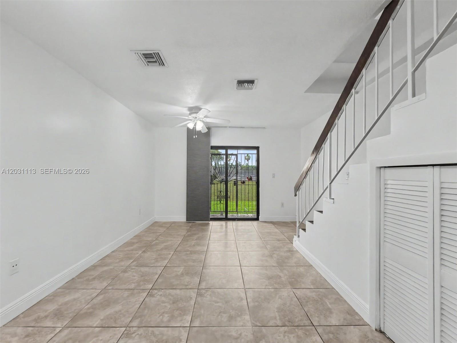 An empty room features tile flooring, a staircase with a wooden railing, and sliding glass doors — 1001 SW 105 Ave # 113, Miami FL 33174, MIAMI, FL