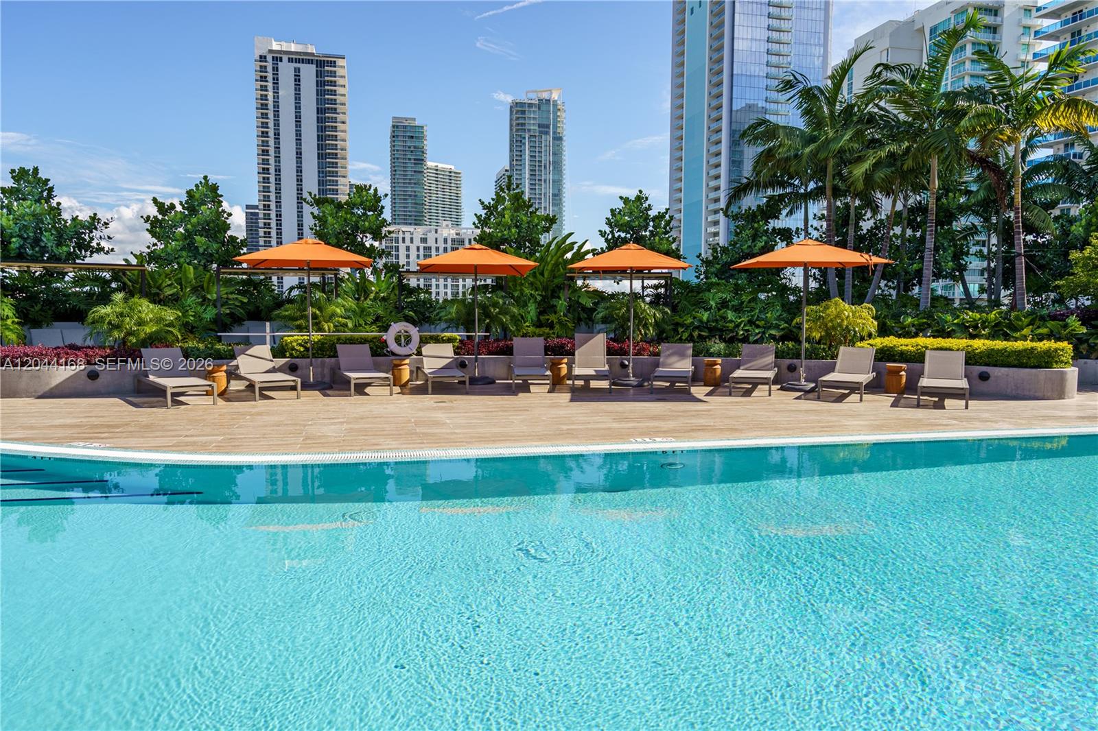 A swimming pool sits in front of a deck with lounge chairs and orange umbrellas — 700 NE 23rd St # 2304, Miami FL 33137, MIAMI, FL