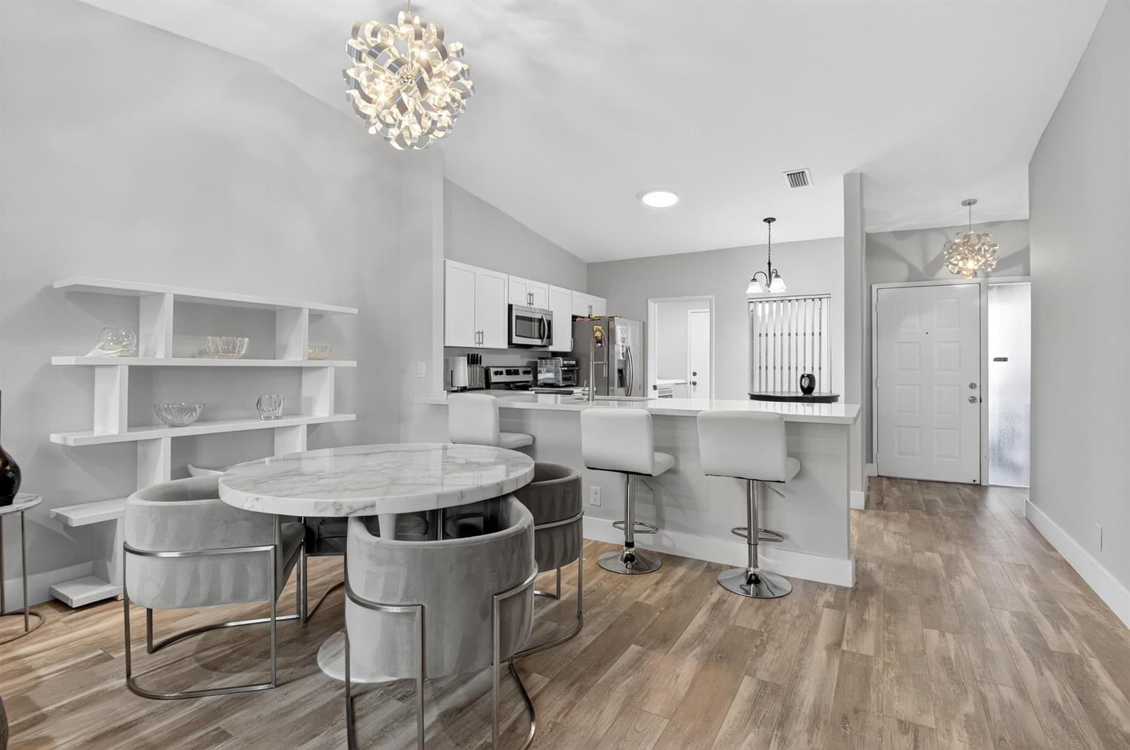A modern kitchen and dining area feature white cabinets, a marble table, and wood flooring — 8256 Summerbreeze Lane, Boca Raton FL 33496, BOCA RATON, FL