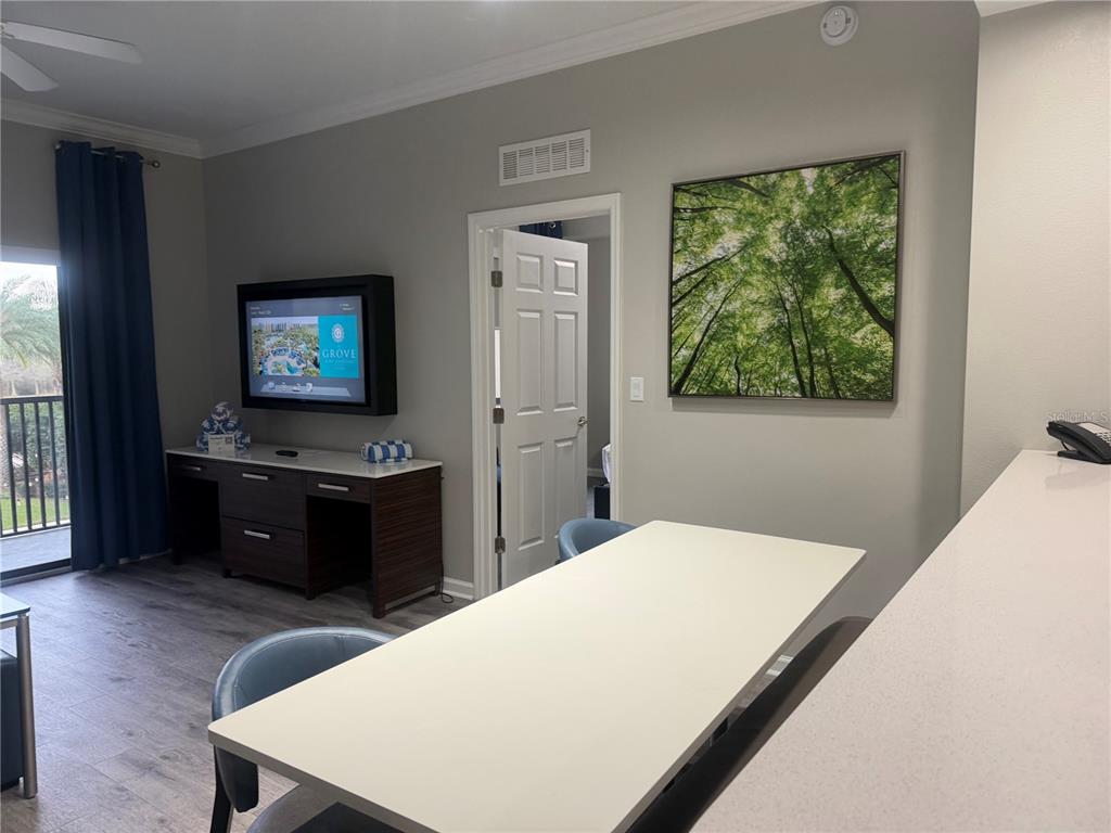 A room features a desk with a wall-mounted television, a dining table, and wall art — 14501 GROVE RESORT AVENUE UNIT 1203, WINTER GARDEN, FL