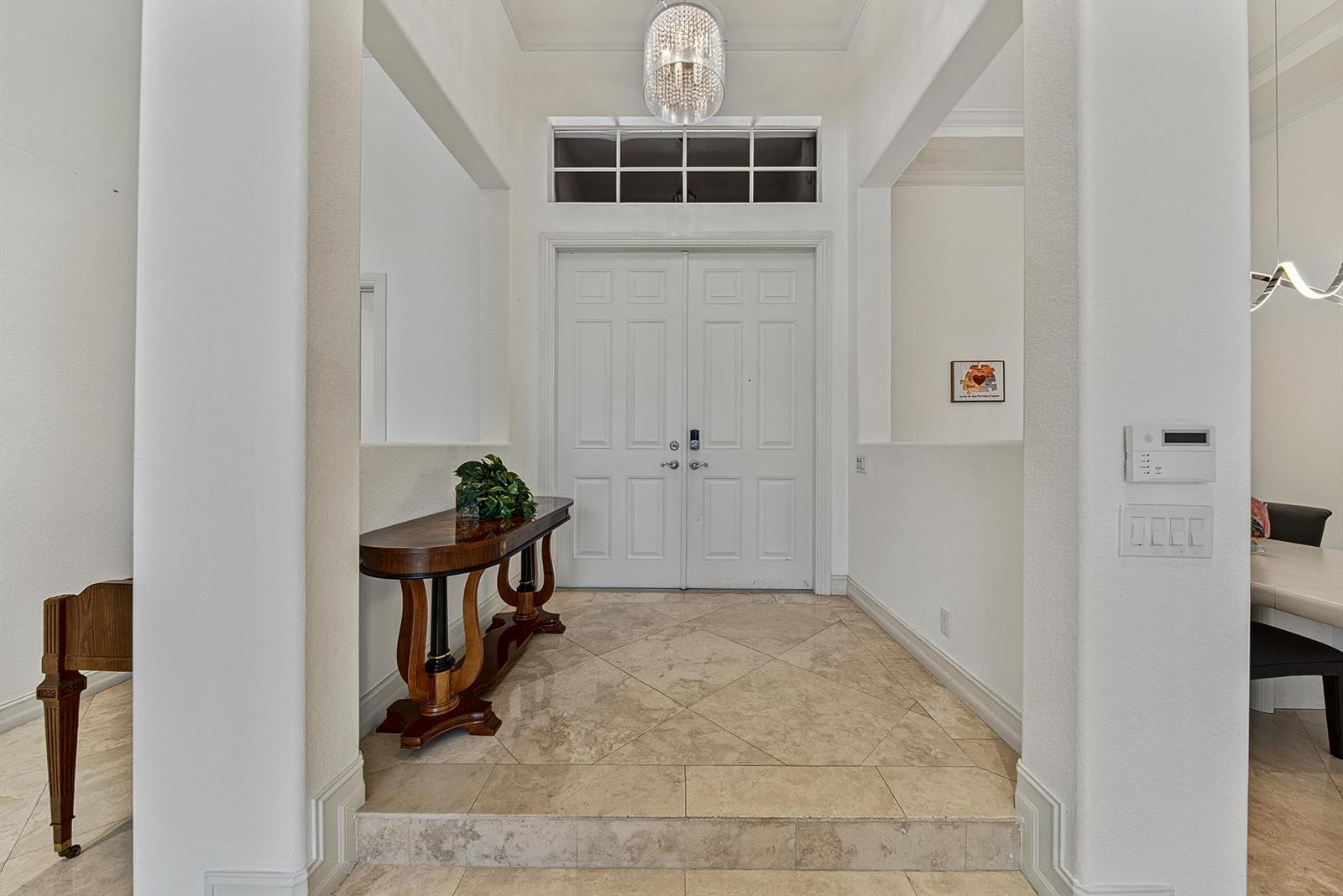 An entryway features a raised tiled floor, a wooden console table, and a crystal chandelier — 7233 NW 123rd Avenue, Parkland FL 33076, PARKLAND, FL