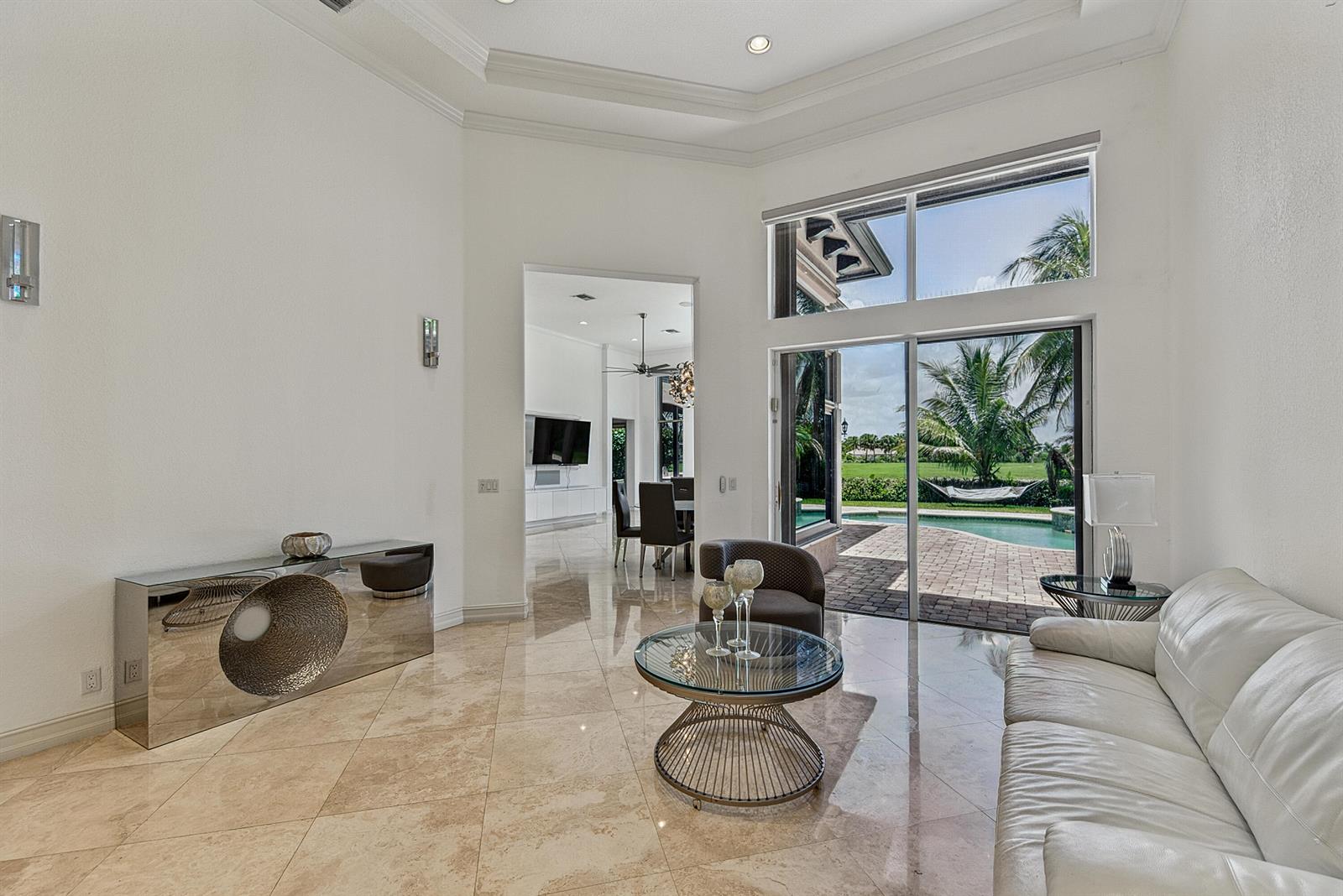 A bright living room with tile floors, a white sofa, and sliding doors to a pool — 7233 NW 123rd Avenue, Parkland FL 33076, PARKLAND, FL