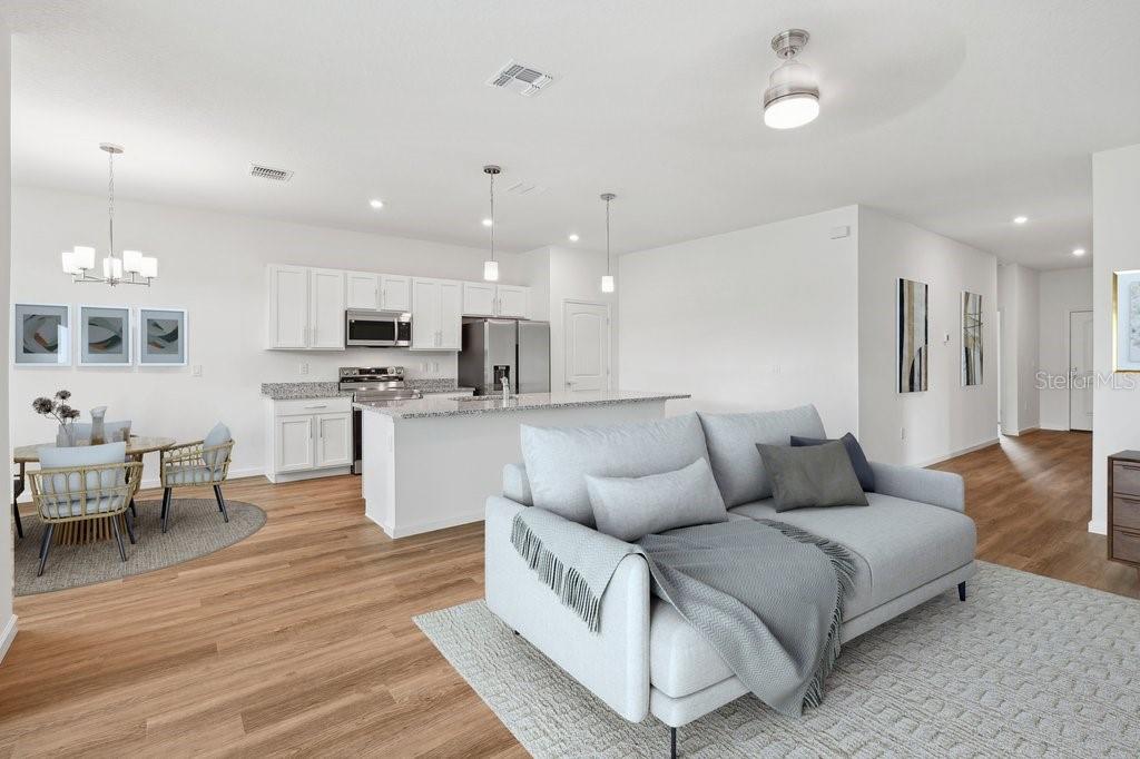 An open-concept living room and kitchen featuring white cabinets, stainless appliances, and wood flooring — 36 RYMER LANE, PALM COAST, FL