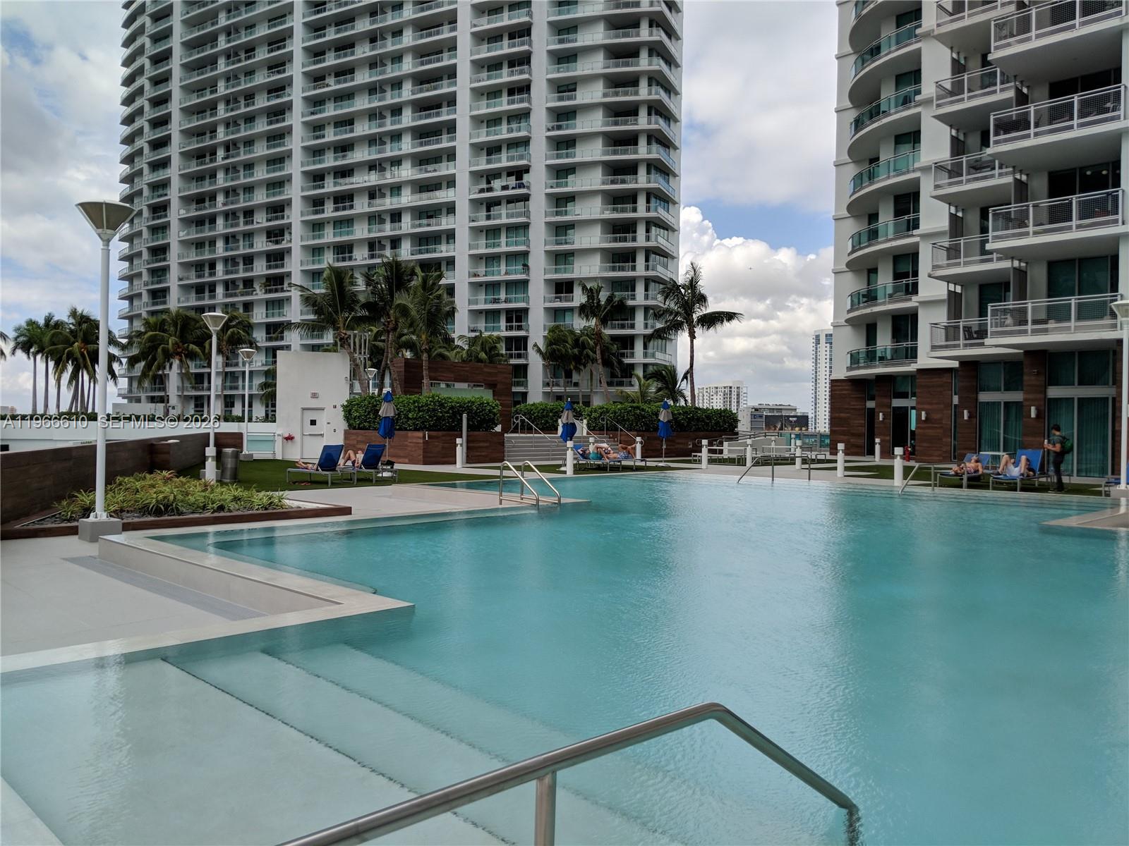 A swimming pool with lounge chairs sits between two tall residential buildings under a cloudy sky — 350 S Miami Ave # 1901, Miami FL 33130, MIAMI, FL
