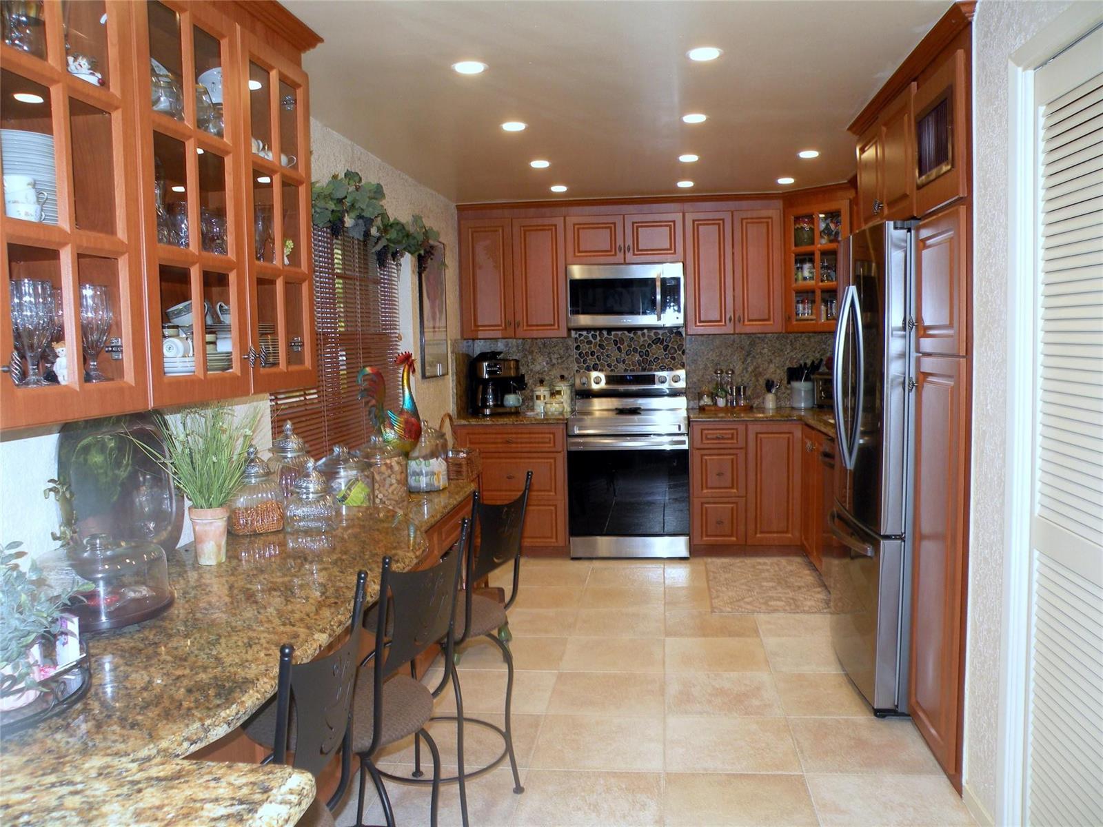 A kitchen features wood cabinets, granite countertops, stainless steel appliances, and a breakfast bar — 4221 W Palm Aire Drive # 102, Pompano Beach FL 33069, POMPANO BEACH, FL