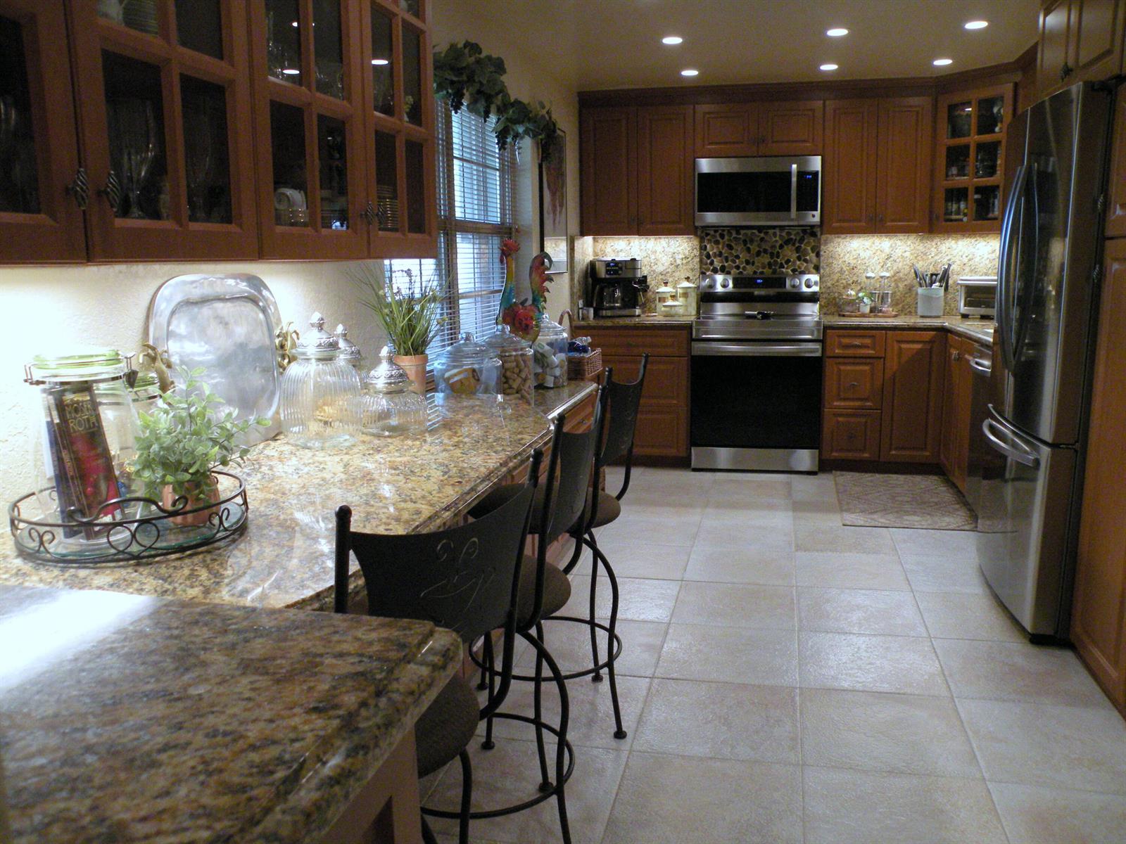 A kitchen features wood cabinets, granite countertops, stainless steel appliances, and a breakfast bar — 4221 W Palm Aire Drive # 102, Pompano Beach FL 33069, POMPANO BEACH, FL