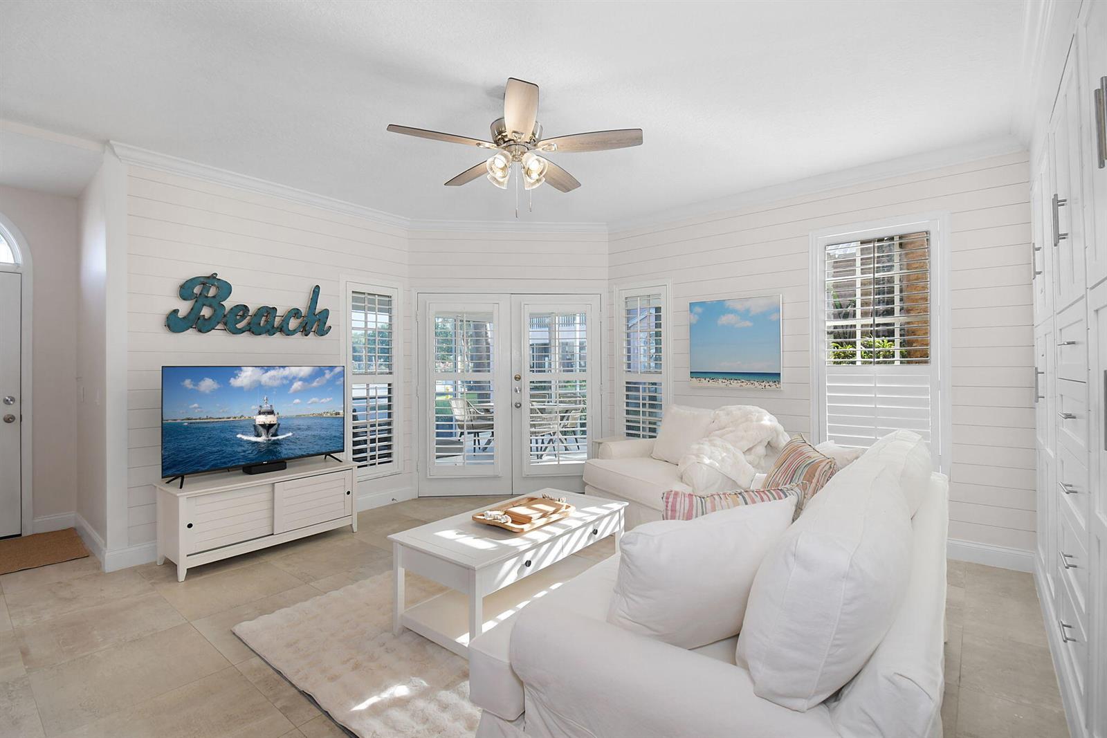A bright living room features white shiplap walls, a white sofa, and a television — 421 NE Plantation # 617, Stuart FL 34996, STUART, FL