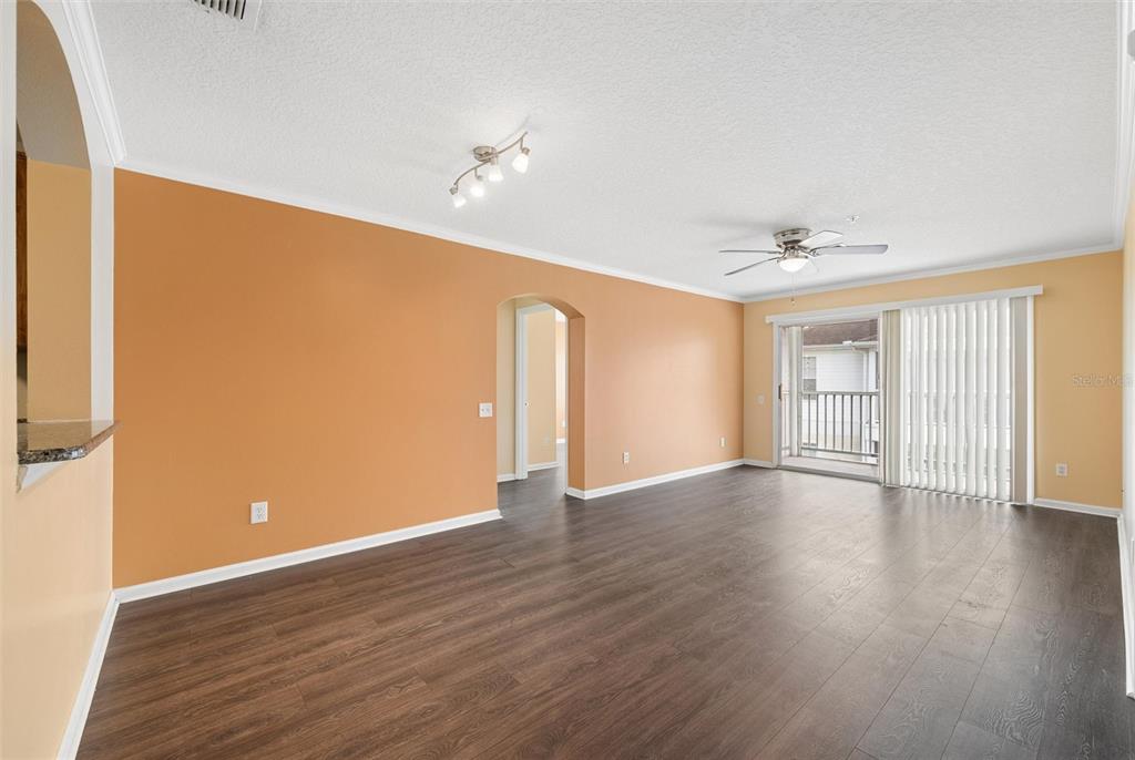 An empty living room with orange walls, dark wood-look flooring, and a sliding glass door — 3930 SOUTHPOINTE DRIVE UNIT 213, ORLANDO, FL