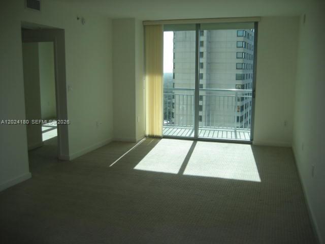 An empty living room with beige carpet, light walls, and a sliding door to a balcony — 9066 SW 73 CT # 1702, Miami FL 33156, MIAMI, FL