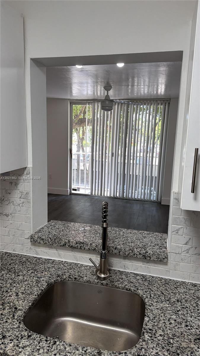 A kitchen sink with a granite countertop and marble-style backsplash overlooks a living area — 1740 NW N River Dr # 325, Miami FL 33125, MIAMI, FL