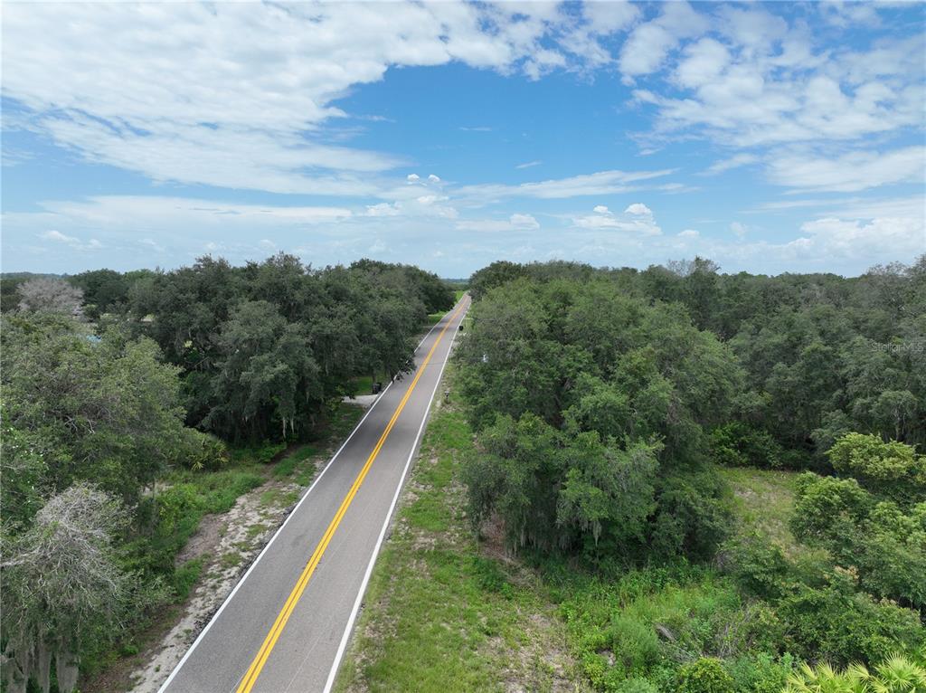 An aerial view shows a paved road stretching through a dense, wooded landscape under clouds — 186 AVON PARK CUTOFF ROAD, FROSTPROOF, FL