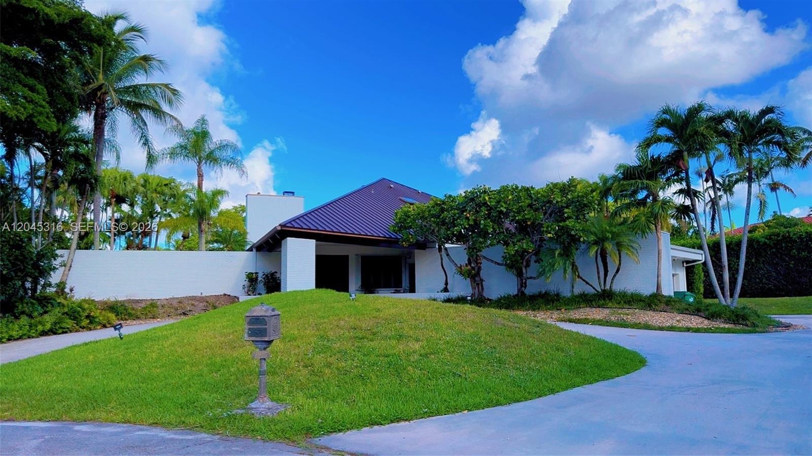 A white brick house with a dark metal roof sits behind a grassy mound — 8925 SW 102nd Ter # 0, Miami FL 33176, MIAMI, FL