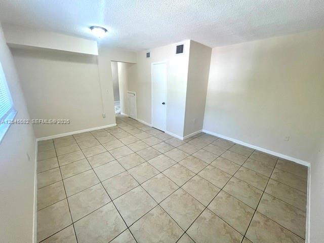 An empty room features light-colored walls, a white door, and beige tiled flooring — 7626 NE 6th Ct # 5, Miami FL 33138, MIAMI, FL